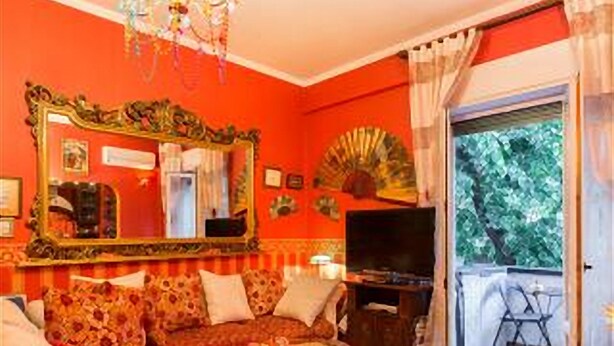A living room with a red wall, a large mirror, a sofa, a television, and a balcony with a view of trees. - ROMANTIC PERFECT FOR CATHEDRAL & EXHIBITION (Milano)
