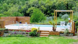 Una terraza de madera con piscina, mobiliario exterior y una pérgola.