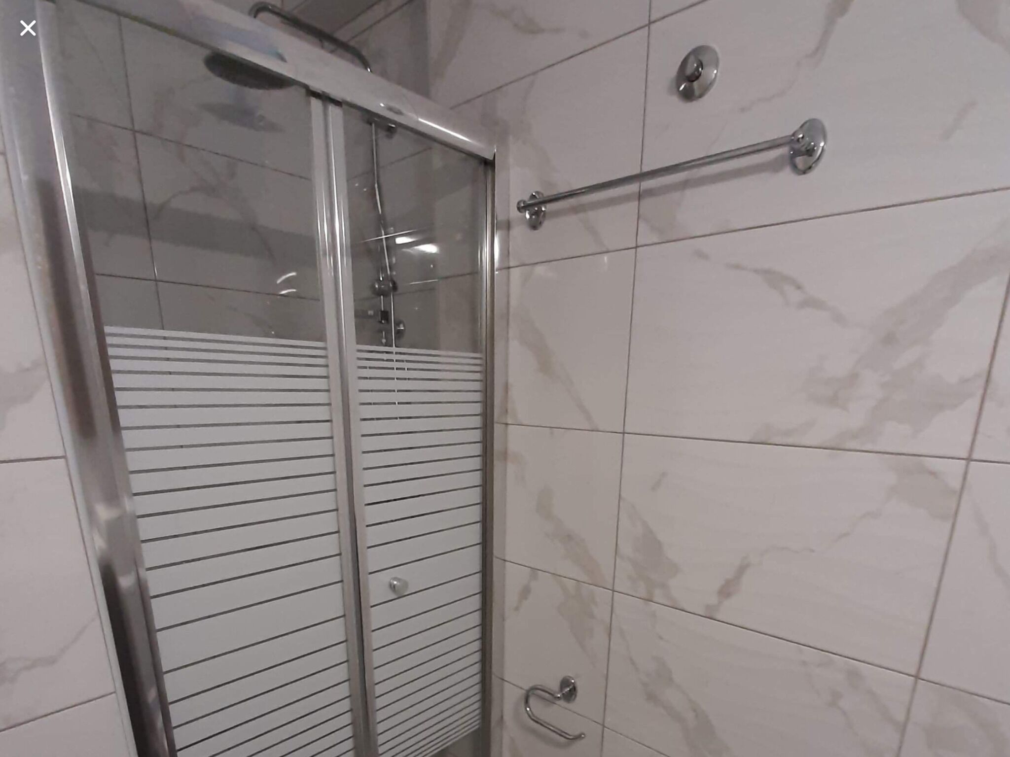 Un baño moderno con cabina de ducha de vidrio, barra de apoyo y pared revestida de mármol.