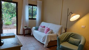 Une pièce avec un lit, un fauteuil vert, une petite table avec une plante et une porte portant l’inscription « SORTIE ».