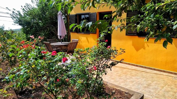 A yellow building with a patio area, a table with chairs, and potted plants.