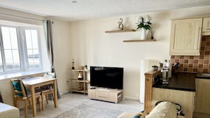 A modern living room with a sofa, TV, wooden shelves, and a dining area with a table and chairs. - Comfy 1 Bed Cardiff Bay Flat With Water Views- WiFi, Millenium Stadium Rugby (Cardiff)