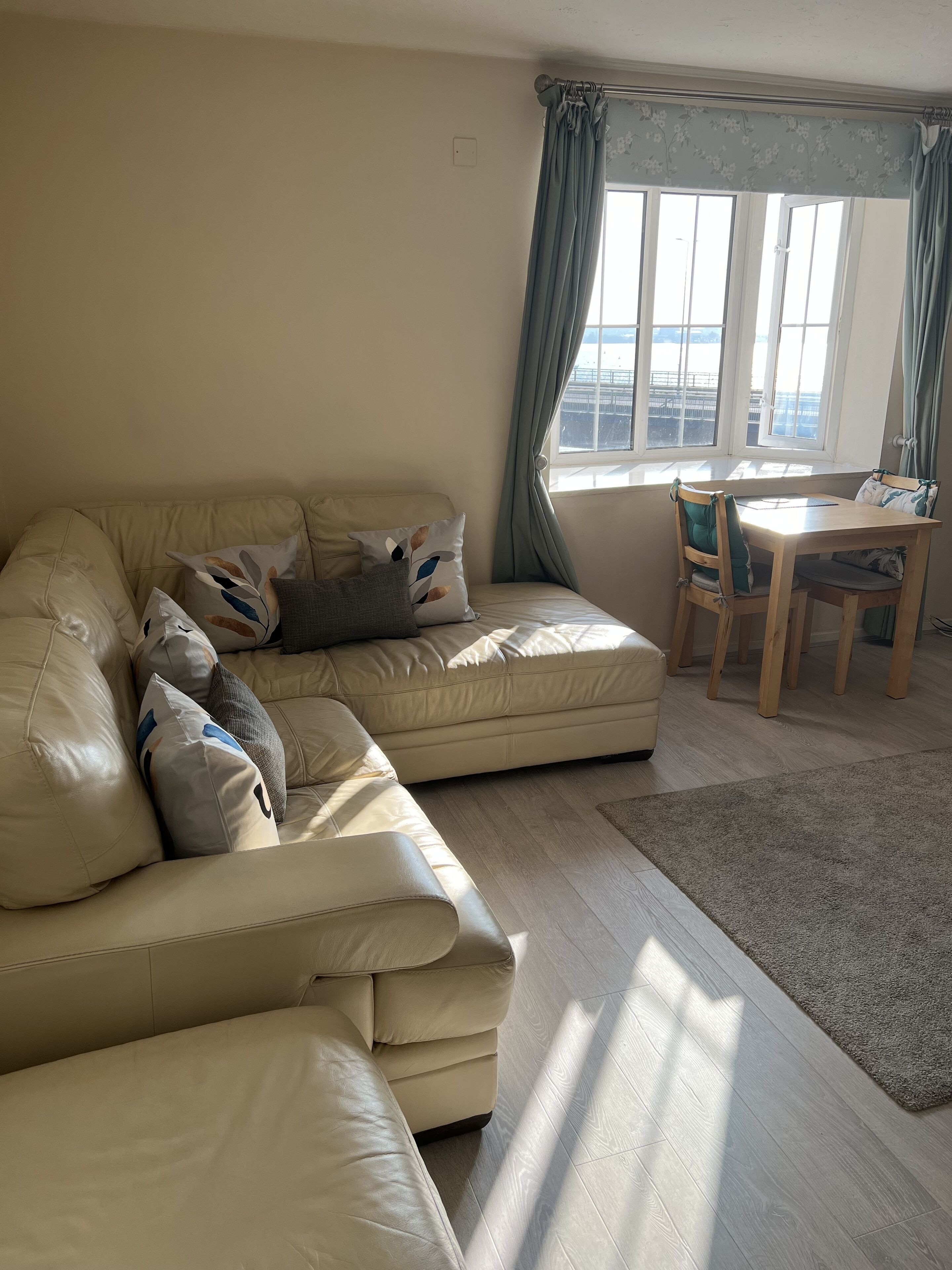 Una sala de estar con un sofá de cuero color beige, una mesa de comedor de madera y vistas al mar a través de amplios ventanales.
