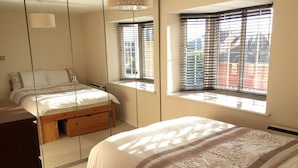 A bedroom with a bed, a dresser, a mirror, and a window with blinds. - Comfy 1 Bed Cardiff Bay Flat With Water Views- WiFi, Millenium Stadium Rugby (Cardiff)