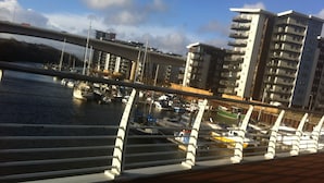 A marina with boats docked, a bridge overhead, and modern buildings in the background. - Comfy 1 Bed Cardiff Bay Flat With Water Views- WiFi, Millenium Stadium Rugby (Cardiff)