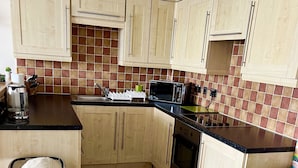 A compact kitchen with wooden cabinets, a microwave, a toaster, and a coffee maker. - Comfy 1 Bed Cardiff Bay Flat With Water Views- WiFi, Millenium Stadium Rugby (Cardiff)