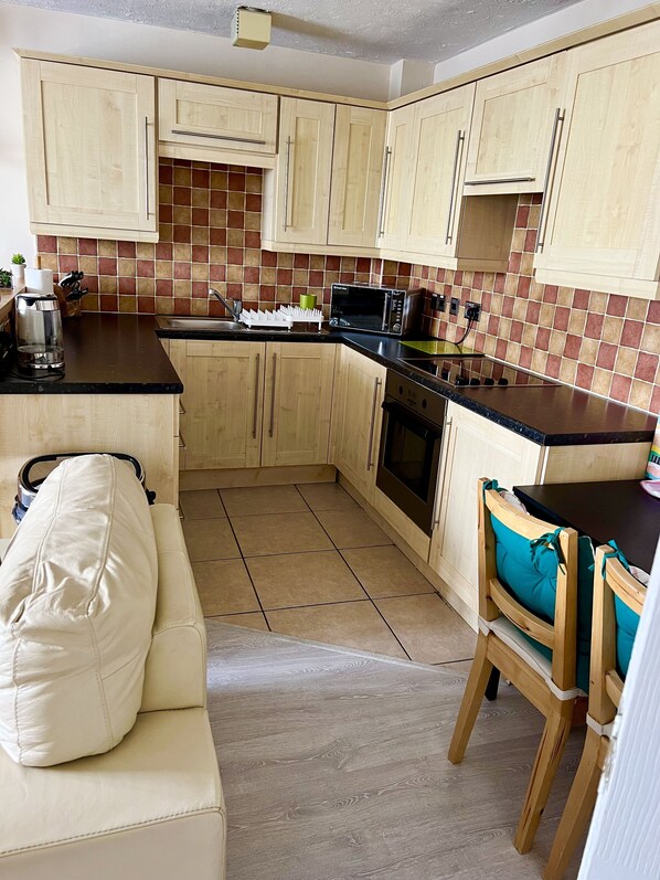 A compact kitchen with wooden cabinets, a microwave, a toaster, and a coffee maker. - Comfy 1 Bed Cardiff Bay Flat With Water Views- WiFi, Millenium Stadium Rugby (Cardiff)