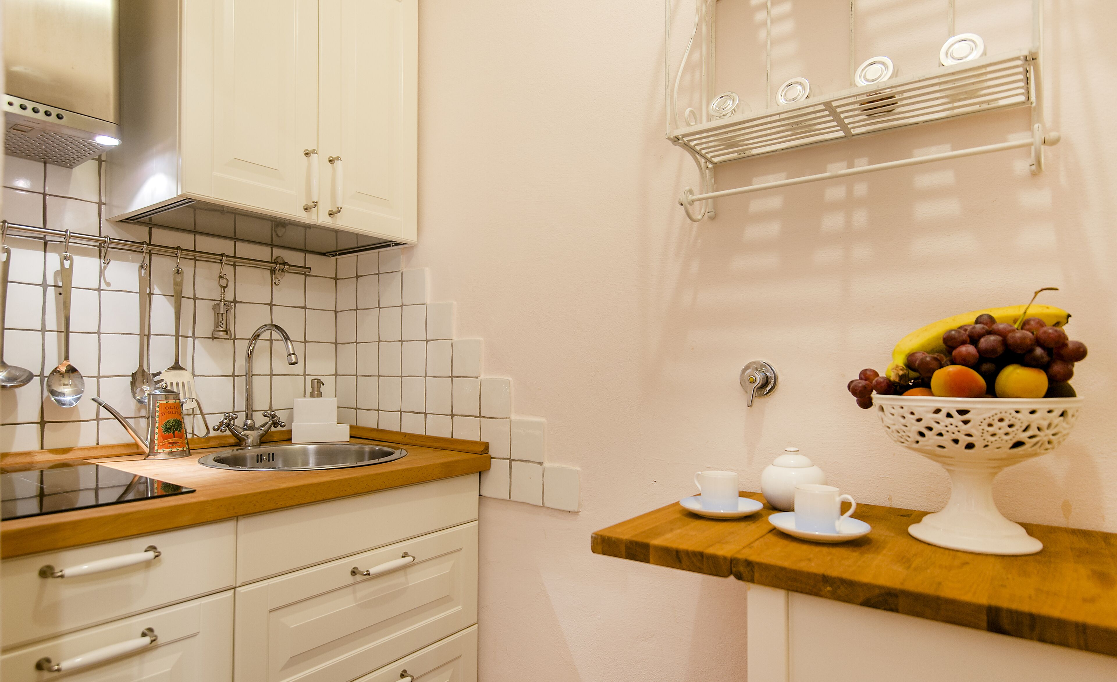 Una cocina con gabinetes blancos, un lavamanos de acero inoxidable y un frutero sobre una repisa de madera.