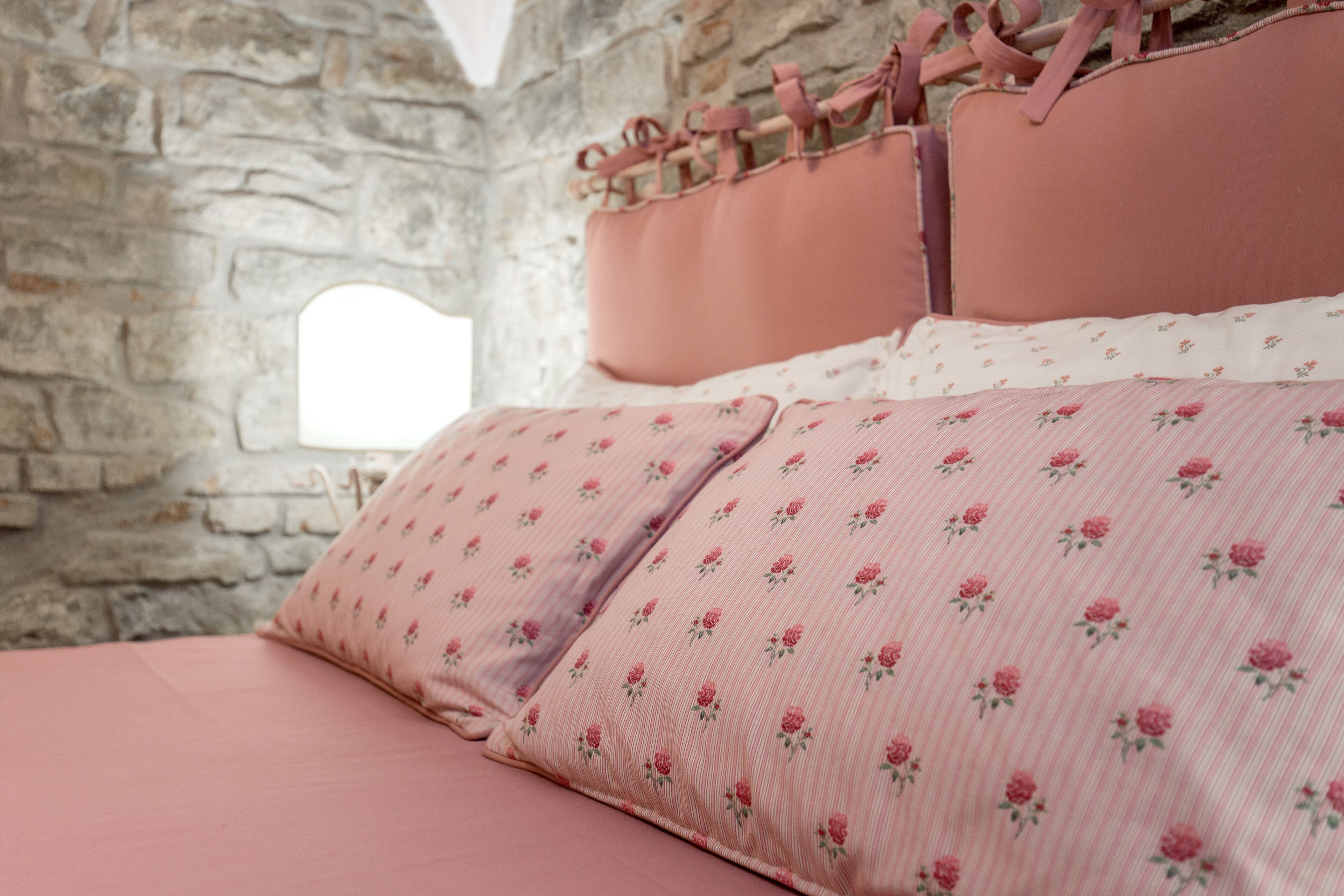 Ein Bett mit rosa Bettwäsche und floralen Mustern, eine Steinwand und ein Fenster.