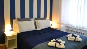 Ein Hotelzimmer mit gestreifter Wand, einem Bett mit weißen und grauen Kissen, einem Nachttisch mit einer Lampe und Handtüchern auf dem Bett.