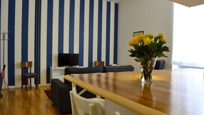 Ein modernes Wohnzimmer mit einem Holzesstisch, einer Sofagarnitur, einem Fernseher und einer Vase mit gelben Blumen.