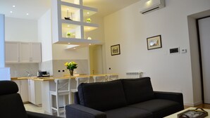 Ein modernes Wohnzimmer mit einer schwarzen Couch, einem weißen Couchtisch und einer Küchenzeile mit weißen Schränken und einer Holz Arbeitsplatte.