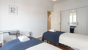 A hotel room with two beds, a desk, a radiator, and a framed picture on the wall. - The ideal place near the Castle * 2BD APT CENTRAL * (Lisboa)