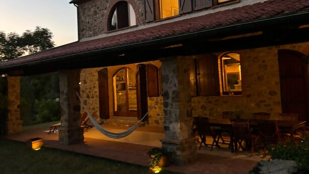A stone building with a tiled roof, multiple windows, and a hammock in the foreground. -  Authentic Massa Marittima Get Away 220 sqm in the Tuscan countryside  (Massa Marittima)