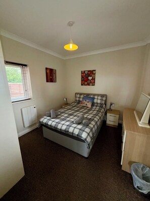 A bedroom with a bed, bedside tables, a desk, a radiator, and a window with blinds. - Seadale Lodge- Holiday rental that sleeps 4-6 people with superb view of Filey (Filey)