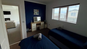 Une chambre avec deux lits, un bureau, une chaise, un téléviseur et une fenêtre avec des stores.