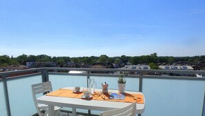 A balcony with a table set for two, overlooking a residential area with houses and trees.