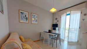 A cozy living room with a sofa, a dining table with chairs, a TV, and a balcony with curtains.