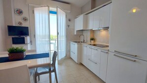 A modern kitchen with white cabinets, a dining area with a table and chairs, and a TV mounted on the wall.
