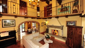 A spacious living area with a fireplace, a piano, and a balcony with a railing.