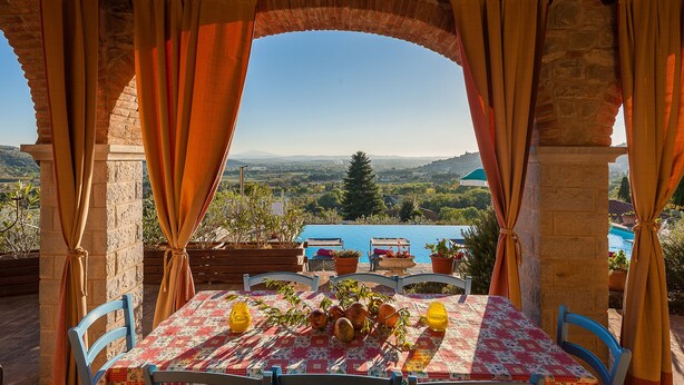 An outdoor dining area with a table set for two, a view of the countryside, and a stone archway.