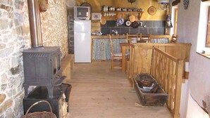 A rustic kitchen with a stone wall, wooden floor, and a stove. There is a refrigerator, wooden chairs, and a counter with various kitchen items. - House in quiet village. Ideal couples, and friends, in Noceda del Bierzo León. (Noceda Del Bierzo León)
