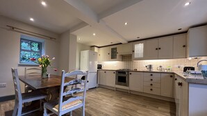 A modern kitchen with wooden flooring, white cabinets, and a dining area with a wooden table and chairs.