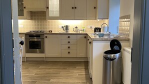 A modern kitchen with wooden flooring, built-in cabinets, a gas stove, oven, and a stainless steel trash bin.