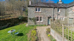 A stone house with a garden, a patio, and a wooden fence.