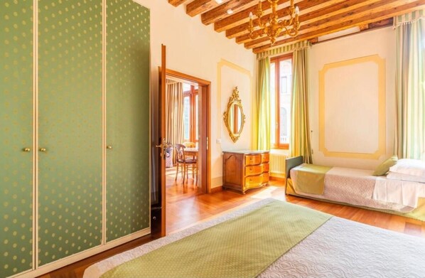 Een kamer met een bed, een dressoir, een spiegel en een raam met gordijnen.