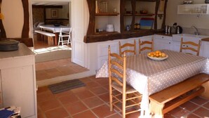 Una cocina con una mesa de comedor, sillas y un banco. Hay una ventana que proporciona luz natural, y un lavamanos con armarios arriba.