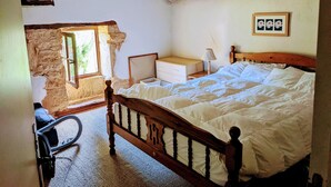 Un dormitorio con una cama de madera, una mesita de noche, un aparador y una ventana con vistas a la vegetación.