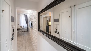 Un pasillo con un espejo que refleja una habitación, un comedor con mesa y sillas, y una pared con textura.