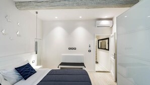 Un dormitorio moderno con cama, mesitas de noche, espejo y un banco empotrado.