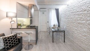 Una cocina moderna con armarios blancos, una campana extractora de acero inoxidable y un comedor con mesa y sillas de vidrio.
