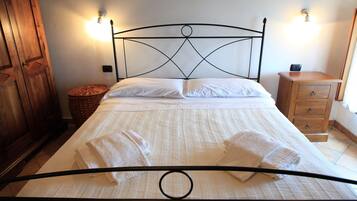 A neatly made bed with white linens and towels, a wooden wardrobe, a wicker basket, and a wooden nightstand with drawers.