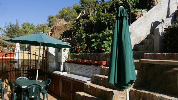 Eine Terrasse im Freien mit Steinstufen, einer Bar und grünen Sonnenschirmen.