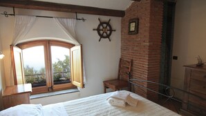 Ein Schlafzimmer mit einem Bett, einem Holzstuhl, einem kleinen Tisch, einem Fenster mit Vorhängen, einer Schiffslenken-Dekoration und einer Ziegelwand.