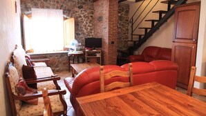 Ein gemütliches Wohnzimmer mit Steinwand, Holzmöbeln, einem Fernseher und einer Treppe.