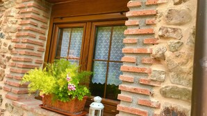 A rustic stone building with a wooden window frame, a potted plant with green foliage and pink flowers, and a white lantern on the ledge. - LA CASA DEL RÍO. Ideal for families with children and couples seeking tranquility (Pujayo)