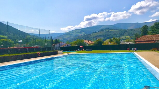 A swimming pool with clear blue water, surrounded by a fence, and set against a backdrop of green hills and a clear sky. - LA CASA DEL RÍO. Ideal for families with children and couples seeking tranquility (Pujayo)