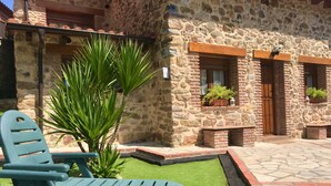 A stone building with a patio area featuring green lawn and two blue chairs. - LA CASA DEL RÍO. Ideal for families with children and couples seeking tranquility (Pujayo)