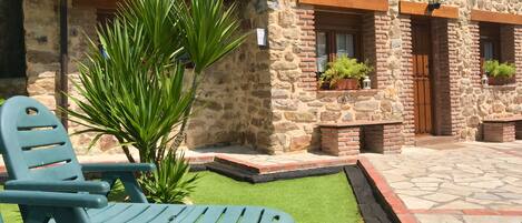 A stone building with a patio area featuring green lawn and two blue chairs.