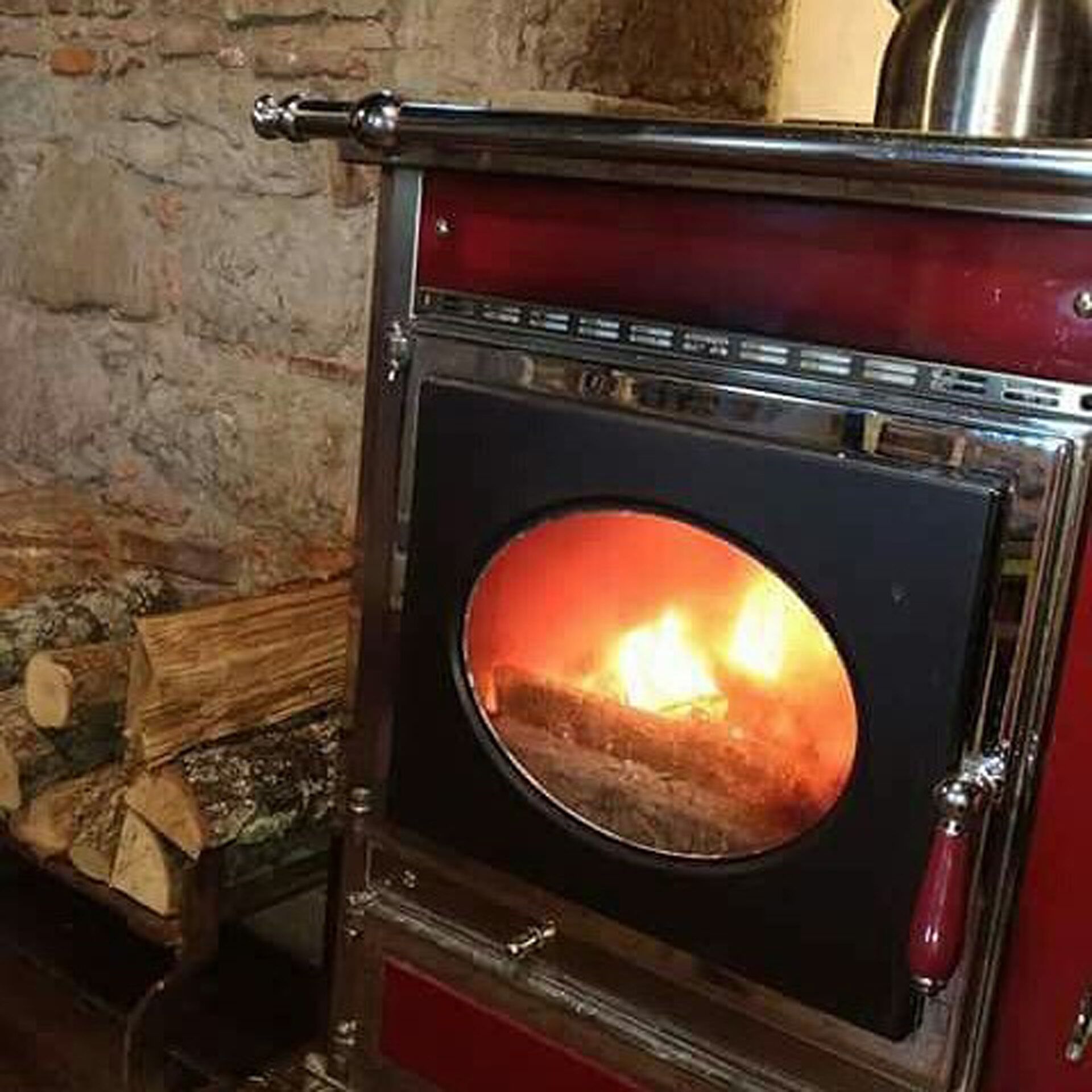 Una estufa de leña con puerta de cristal, frente a una pared de piedra.