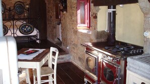 A rustic kitchen with a vintage stove, a wooden table with chairs, and a stone wall.