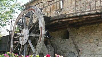 Traditional stone building with a historic water wheel and lush surroundings.