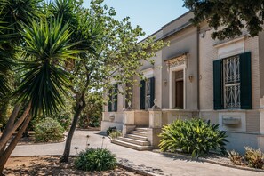 A building with a stone facade, green shutters, and a central entrance with steps.