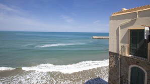 Um edifício costeiro com fachada de pedra, varanda com guarda-corpo e vista para o mar.