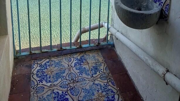 Varanda com vista ampla para o mar, um vaso de planta, um azulejo decorativo e uma bacia de pedra.