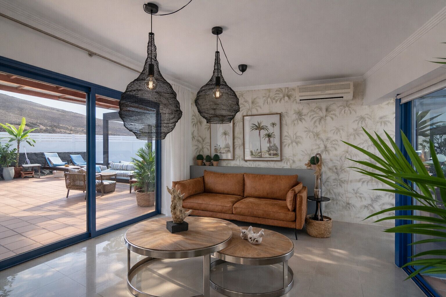 Un salon moderne avec un canapé marron, deux tables rondes et des luminaires suspendus.